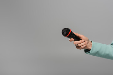 Cropped view of hand of host of event in blue jacket holding black and wireless microphone during holiday while standing isolated on grey