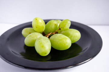 Fresh green grapes on a black plate on a white background