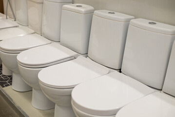 Ceramic toilet bowls of different types on a shop window. Sale of sanitary equipment in a...