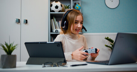 Caucasian 10 years old girl gamer playing video games at home. Happy girl gamer wear headphone competition play video game online on laptop in living room at home. © serg