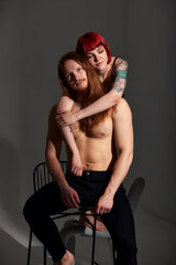 Studio portrait of a sexy half-naked couple in love. A woman with red hair and a colored tattoo gently hugs her handsome man with long hair and a beard. Love, passion and tenderness.