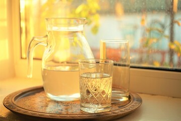 A jug of water and two glasses in a wooden tray on the windowsill.