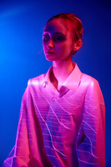 Power. Portrait of young girl in white blouse with neon filter reflection posing against blue...