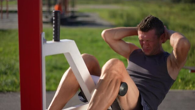 Exhausted adult man finish crunches on exercise bench sighing wiping perspiration off face. Portrait of tired motivated Caucasian sportsman working out on sunny day outdoors