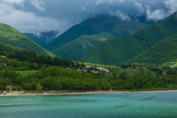 View of little mountain village over Fiastra lake with mountains in the background - 603289183