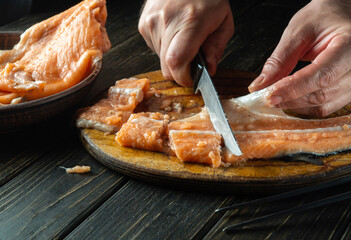 Cutting red fish with a knife on a kitchen cutting board before cooking. Close-up of hands of a chef while cleaning raw fish.