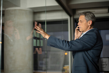 Portrait of successful businessman in office. Man writing on the glass board in office. Businessman talking to the phone.
