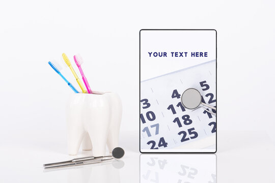 Dentist appointment date or any other dental message on tablet, ceramic tooth with three bright colors toothbrushes and dental tools mock up. White background.