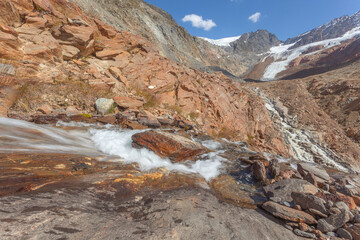 Mountain stream over rocks smoothed by the Vallelunga Glacier seen in the background. The glacier is in rapid retreat occurred due to global warming, Alto Adige, Italy