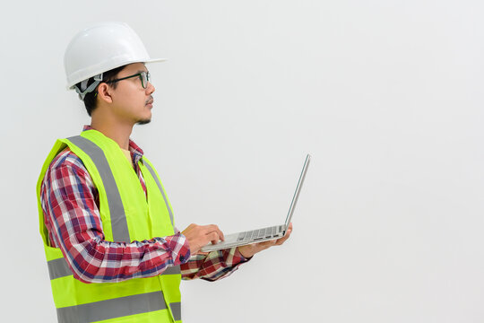 Asian Male Architect Or Engineer Wearing White Hard Hat Holding Laptop Isolated On White Background Copy Space Over A White Studio Background.