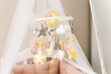 Fototapeta na wymiar Toys over the crib. A mobile baby cot with stars, clouds and a unicorn.