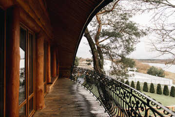 Obraz premium A large semicircular balcony of a wooden house with wrought iron railings and a beautiful view of nature and the river