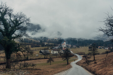 A captivating winter scene featuring a mountain road leading to a charming small town nestled among fog-covered mountains in Slovenia. 