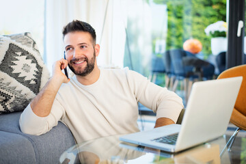 MId aged man wearing casual clothes and having a call and using laptop at home