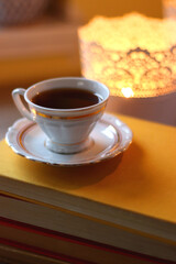 Cup of tea or coffee, plate of cookies, books, e-reader, pencil and lit candles on the table. Selective focus.
