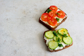 A sandwich with cucumber,  tomato and chopped parsley on a grey table, copy space