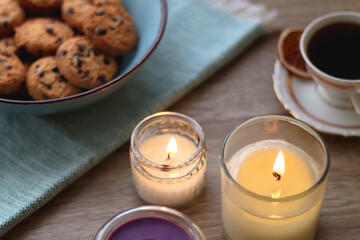 Plate of chocolate pralines, bowl of cookies, cups of tea, glasses of juice and lit candles on the table. Selective focus.