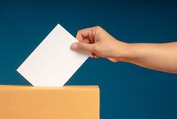 Election day. Hand voter holding ballot paper putting into the voting box at place election against a blue background