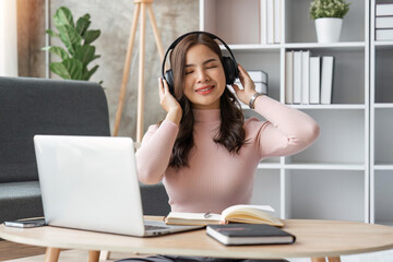 Naklejka premium Young woman using laptop at home, listens music through headphones. Beautiful smiling girl sitting on the sofa