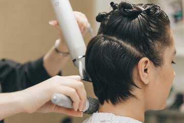 Naklejka premium Close-up of the hands of a hairdresser drying women's hair with a hairdryer. short haircut and styling