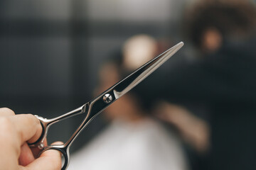 Obraz premium scissors in hands, in the background a hairdresser makes a haircut to a woman, a beauty salon