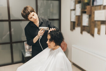 Close-up of the hands of a hairdresser drying women's hair with a hairdryer. short haircut and styling