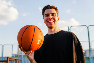 Young brunette man holding basketball ball looking positive and happy standing and smiling with a confident smile showing teeth