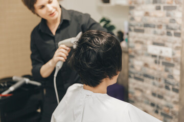 Obraz premium Close-up of the hands of a hairdresser drying women's hair with a hairdryer. short haircut and styling