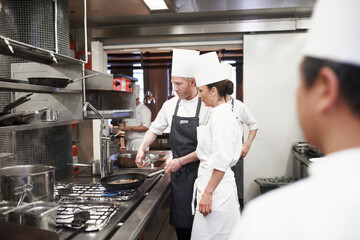 Chef, teamwork and people with frying pan in kitchen, catering service and prepare food for fine...