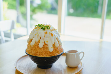 Japanese shaved ice dessert , milk tea kakigori bingsu topped with sweet whipping cream almond stick Thai tea sauce condensed milk on table in cafe. Traditional summer dessert menu in Japan.