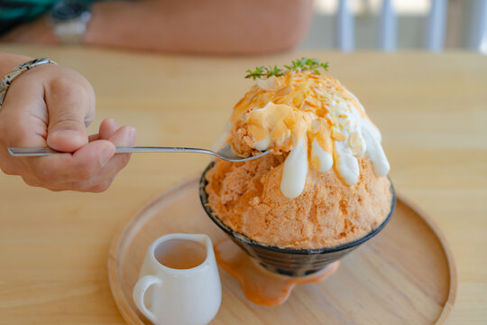 Closeup eating sweet milk tea kakigori bingsu. Japanese shaved ice dessert with Thai tea sauce on whipping cream topped with almond slide condensed milk. Traditional summer dessert in Japan.