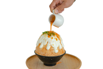 Japanese shaved ice dessert , Hand pouring sweet Thai tea sauce on whipping cream. Served with milk tea kakigori bingsu topped with almond slide condensed milk. Traditional summer dessert in Japan.