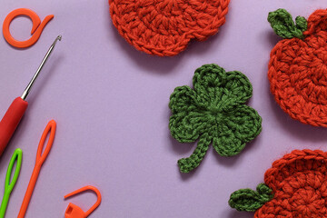 Crochet clover leaf and orange pumpkin and crochet accessories on a violet background. Top view. Copy space.