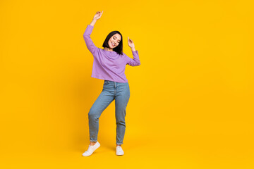 Fototapeta na wymiar Full length photo of good mood woman wear purple shirt jeans shoes enjoy dancing raising hands isolated on yellow color background