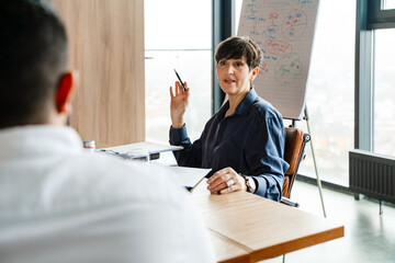 Professional elderly confident businesswoman talking to colleague at office meeting 