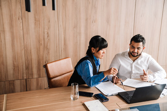 Pretty multinational team gathered around table while discussing project on laptop in office