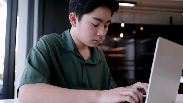 Education everywhere learning concept, Asian boy doing homework or chatting to colleage by using Technology laptop computer, teenager highschool student studies  alone in co-working space indoors