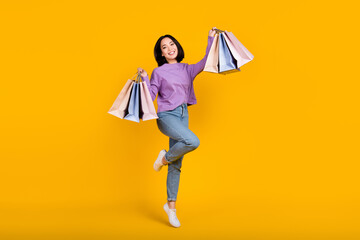 Full length photo of cheerful excited woman wear violet shirt rising shoppers isolated yellow color...