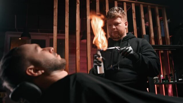 Skilled male barber spraying sharp razor fire burning flame customer beard shaving barbershop slowmo