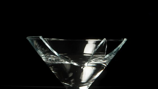 A broken martini cocktail glass on a black background, dolly slider extreme close-up.