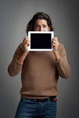 Tablet screen, mockup and portrait of man peeking in studio isolated on a gray background. Touchscreen, scared and male person with space for marketing, advertising and technology for promotion.