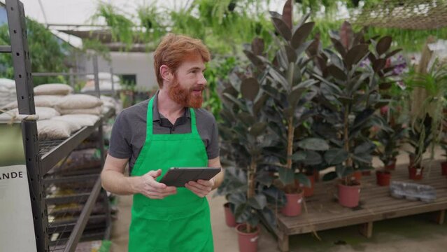 Employee in Green Apron Using Tablet for Inventory While Roaming Flower Shop. Young Man's Tech-Driven Local Business Operations