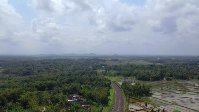 Aerial view of the train run past the countryside with cloudy sky during the day. The train run away from the camera. Train trip path with beautiful views, Indonesia - 4K drone footage