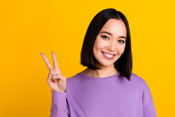 Photo of shiny charming woman wear violet shirt showing v-sign smiling empty space isolated yellow color background