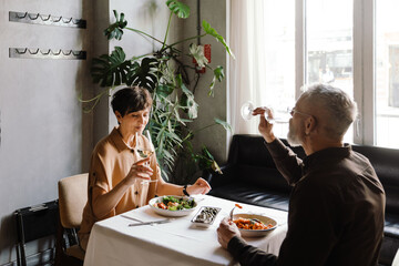 Positive mature couple dining and drinking glasses of wine in cafe