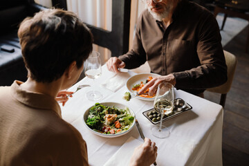 Back view of mature couple dining with glasses of wine in cafe