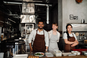 Cheerful multiethnic chefs looking at camera while standing in kitchen