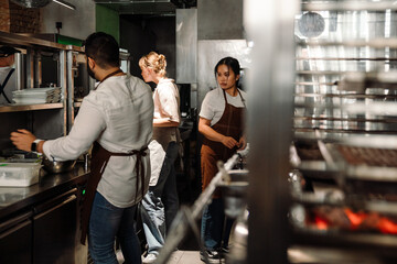 Back view of three serious multinational chefs prepare healthy food in kitchen