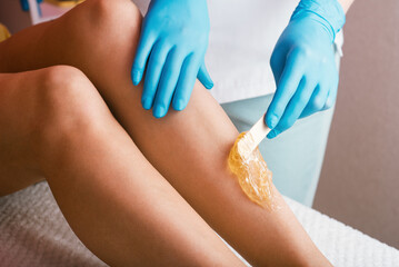Hands of a cosmetologist close-up, in blue gloves, applying sugar paste on a woman's leg. Depilation procedure