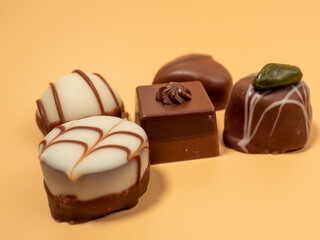 Assorted gourmet pralines in white, dark and milk chocolate. Chocolate candies on an orange background.